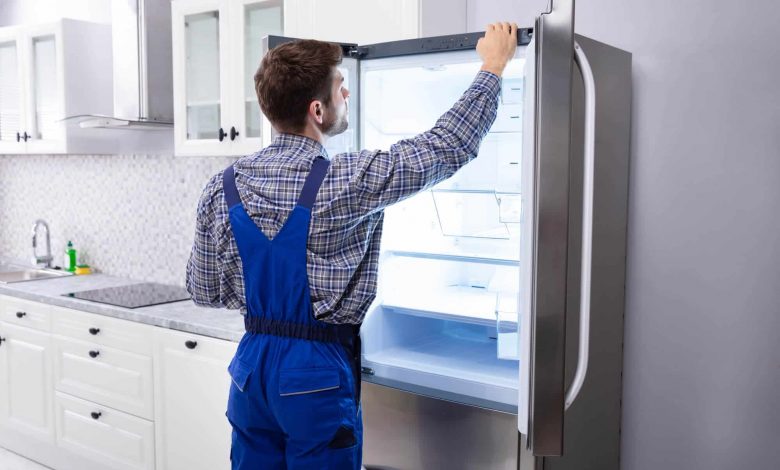 Serviceman Checking Temperature Of Refrigerator In Kitchen