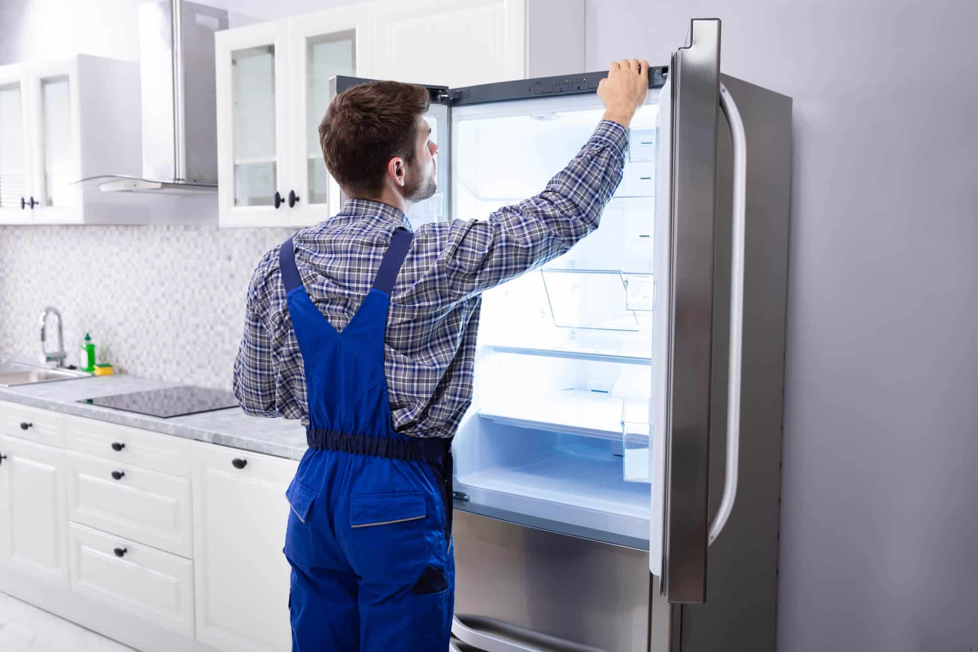 Serviceman Checking Temperature Of Refrigerator In Kitchen