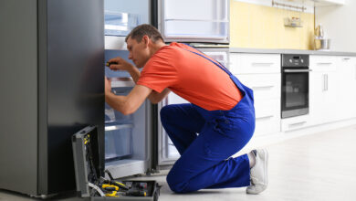 Male Technician With Screwdriver Repairing Refrigerator in Kitchen