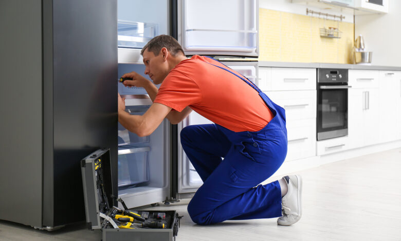 Male Technician With Screwdriver Repairing Refrigerator in Kitchen
