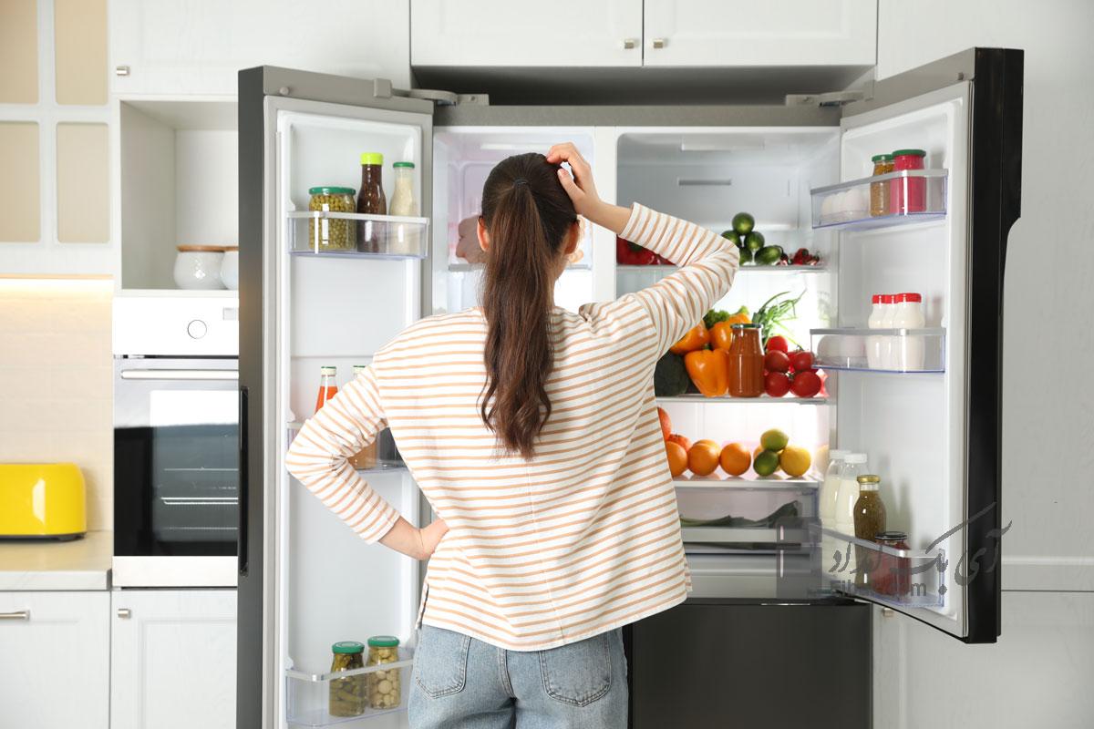 Young woman near open refrigerator in kitchen back view